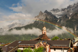 Regenbogen über dem Kirchturm von Mittenwald im bayrischen Karwendel. Im Hintergrund das teilweise schnee bedeckte westliche Karwendelgebirge. Regenbogen über dem Kirchturm von Mittenwald im bayrischen Karwendel. Im Hintergrund das teilweise schnee bedeckte westliche Karwendelgebirge.